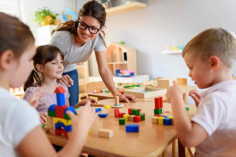 Early years educator and children playing with colourful didactic wooden toys in a nursery setting